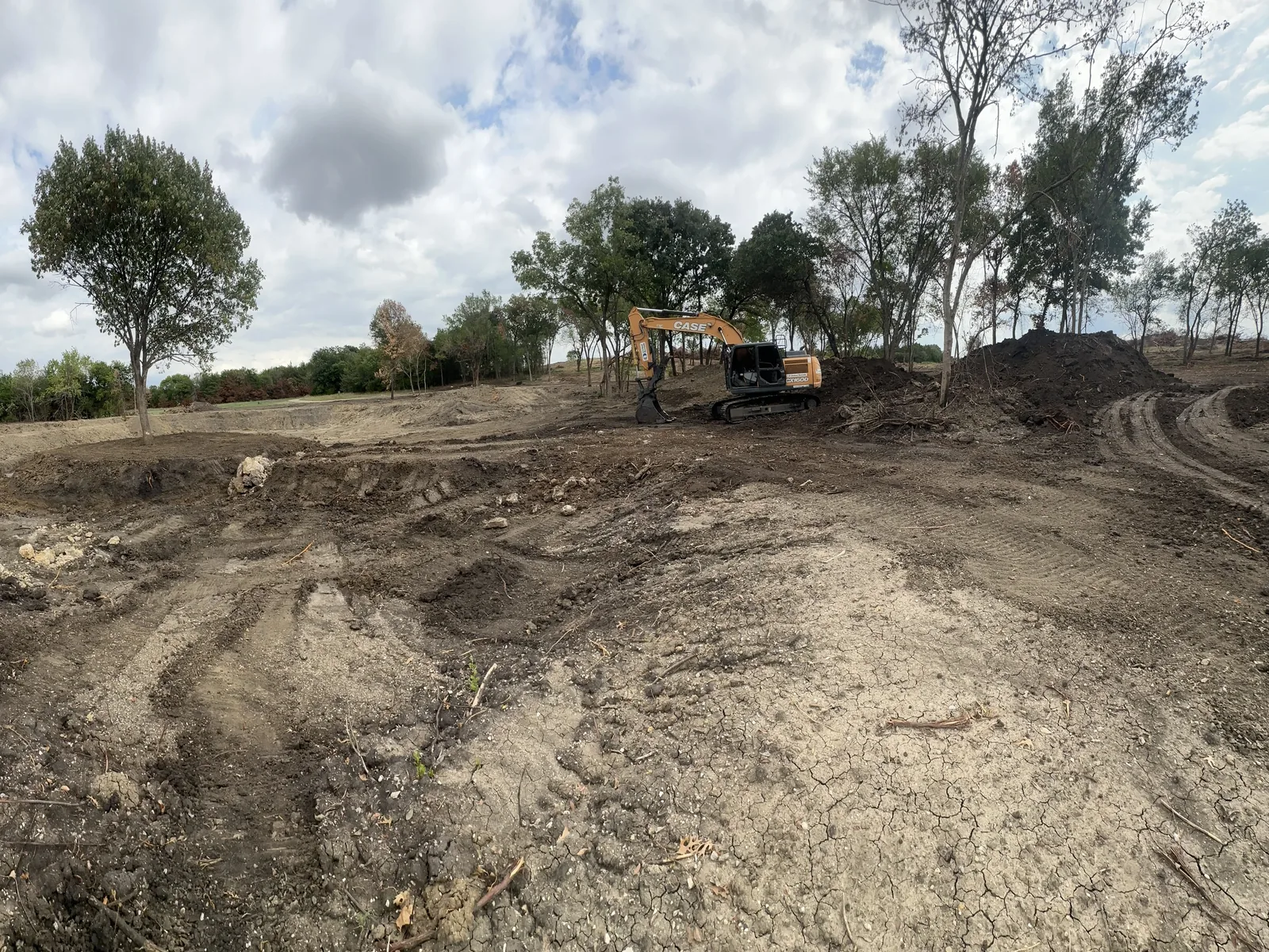 Excavator cutting the pond basin with rock and spoil piled to the side